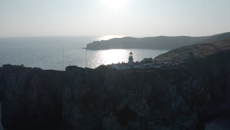 Toma-Aérea-Lenta-Del-Complejo-De-Edificios-Del-Faro-De-Gamov,-De-Pie-Sobre-Un-Acantilado-Rocoso-Empinado,-Al-Atardecer