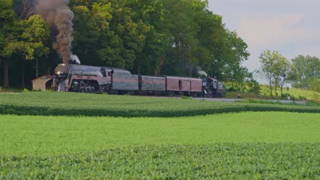 Una-Vista-Aérea-De-Un-Tren-De-Vapor-No-611-Que-Sopla-Humo-A-Través-Del-Campo-Agrícola-En-Un-Día-Soleado-De-Verano-Con-Campos-Verdes