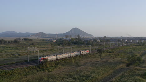 Russische-Eisenbahnlokomotiven-Bewegen-Sich-Durch-Grüne-Felder-Mit-Bergen-Im-Fernen-Hintergrund-Bei-Sonnenuntergang,-Russische-Föderation