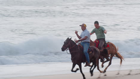 Slow-Motion-Following-Close-Shot-of-Two-Men-Horseback-Riding-Galloping-along-the-Beach-in-Tambor,-Costa-Rica