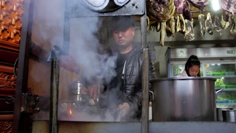 Male-preparing-food-over-smoking-flames-at-Shaxizhen-Shaxi-village-outdoor-market