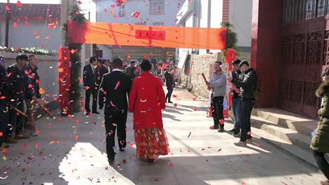 Chinesisches-Hochzeitspaar,-Das-In-Zeitlupe-Die-Straße-Hinuntergeht,-Während-Ein-Konfetti-Feuerwerk-Durch-Die-Szene-Hinter-Ihnen-Schwebt