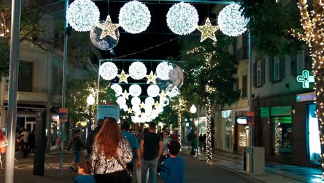 Various-people-walking-at-night-through-downtown-city-streets-decorated-for-the-festive-season-with-chirstmas-lights-at-Madeira-Island---Portugal-celebrating-xmas-color-graded-HD-background