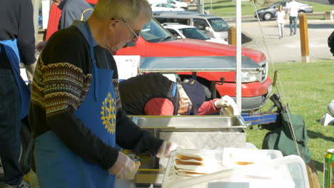 Volunteer-Elderly-Male-Serving-Sausages-At-A-Fundraiser