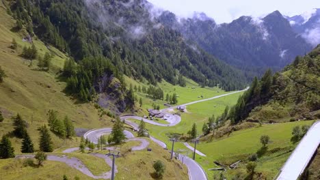 Winding-road-goes-up-the-mountain-at-the-Dolomite-park-in-northern-Italy-with-cable-cars-visible-going-up-the-tram,-Aerial-drone-pedestal-lift-shot