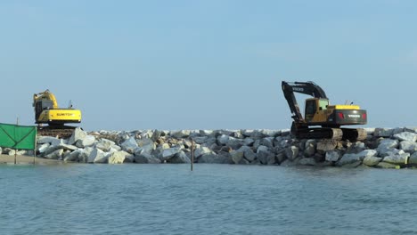 Two-large-yellow-excavators-building-a-rock-wall-to-stop-erosion-of-the-beaches-and-keep-large-waves-and-storms-from-destroying-the-coastline