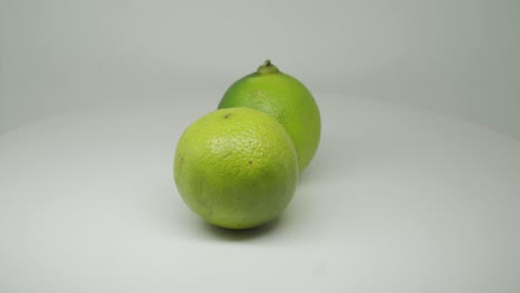 Grüne-Zitrusfrüchte-Reife-Limette,-Die-Sich-Im-Uhrzeigersinn-Auf-Dem-Tisch-Mit-Weißem-Hintergrund-Dreht---Nahaufnahme