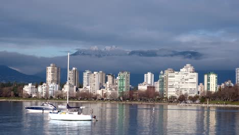 Little-boat-going-across-the-frame-with-two-other-boats-anchored-off-English-Bay-close-to-downtown-Vancouver-on-a-sunny-winter-day-with-snowy-peaks-and-clouds-in-the-background