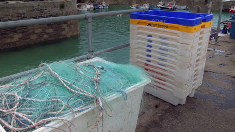 Redes-De-Pesca-Y-Cajas-En-El-Puerto-Con-Barcos-En-El-Fondo