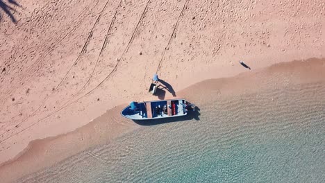 clockwise-rotating-drone-shot-of-Africans-filling-up-a-small-boat-with-diving-bottles-from-a-wheelbarrow-on-a-tropical-sand-beach-in-the-Comoros,-Africa
