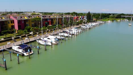 Boat-filled-marina-and-rows-of-beach-homes-line-the-pier-entrance-to-the-harbor,-Aerial-drone-flyover-shot