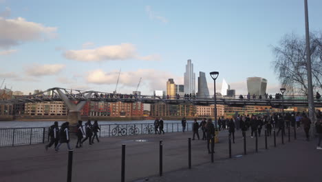 View-of-people-passing-under-Millenium-Bridge-with-skyscraper-skyline-of-the-city