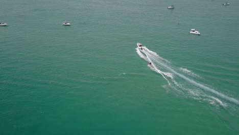 Tracking-aerial:-man-on-red-surfboard-waterskies-on-green-lagoon-water
