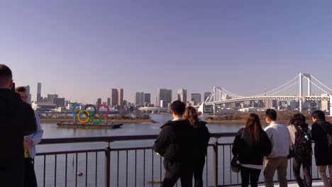People-standing-by-the-esplanade-taking-pictures-in-Tokyo-Bay-where-the-famous-Olympic-sign-is-displayed---medium-shot