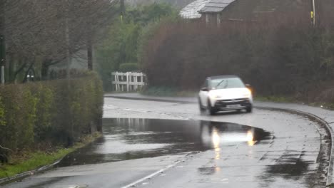 Vehicles-driving-on-stormy-flash-flooded-country-road-bend-UK
