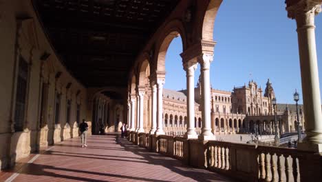 Following-man-in-covered-walkway-of-Plaza-de-Espana-in-Seville,-Spain