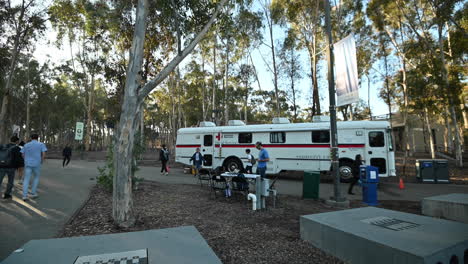 Red-Cross-Bus-At-University-of-California-San-Diego-With-Student-Crossing-In-The-Pathway---Wide-Shot
