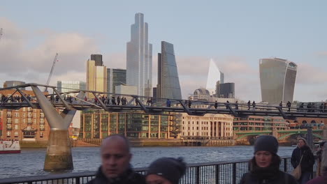 People-walking-over-Millenium-Bridge-in-front-of-business-corporate-office-skyline