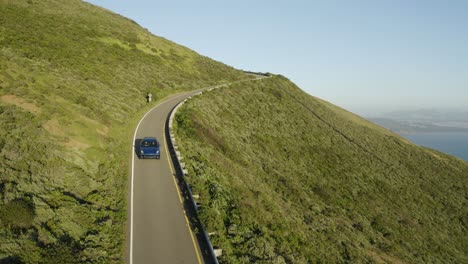 Blue-Porsche-Macan-driving-down-a-coastal-road-in-the-Marin-Headlands-of-San-Fransisco,-California