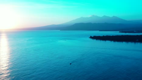 Tranquil-sea-surface-reflecting-glowing-sunset-with-bright-blue-sky-over-mountain-horizon-of-tropical-islands-in-Indonesia