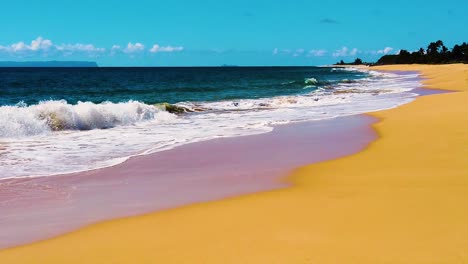 HD-Hawaii-Kauai-slow-motion-static-wide-shot-with-beach-along-bottom-and-right-frame-with-ocean-waves-crashing-and-washing-in-from-left-to-right-edge-of-frame-with-an-island-in-distant-left-frame