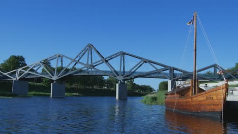 Altes-Segelboot-Aus-Holz,-Das-Neben-Der-Modernen-Fußgängerbrücke-Aus-Metall-In-Kedainiai,-Litauen,-Festgemacht-Ist