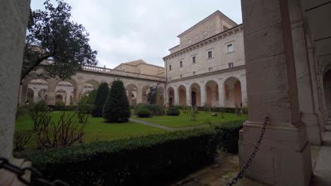 View-of-inner-courtyard-at-abbey-of-Montecassino-with-arches-and-green-foliage,-Italy,-handheld-pan