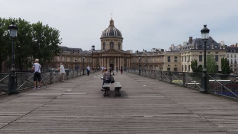 Puente-Pont-Des-Arts-Con-Pocas-Personas-Caminando-Y-El-Instituto-Francés-En-El-Fondo,-Gran-Tiro-Inclinado-Hacia-Arriba-Durante-El-Día-De-Verano-En-París,-Francia