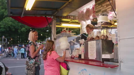 Mother-and-daughter-buying-cotton-candy-from-carnival-food-vendor,-Tilt-Down,-Pan-Left