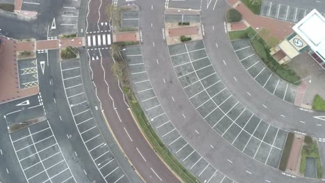 Aerial-view-above-urban-shopping-centre-empty-parking-spaces-closed-COVID-virus-town-lock-down-rotating-birds-eye