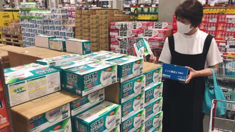 Japanische-Frau,-Die-Eine-Maske-Im-Supermarkt-Trägt-Und-Masken-Vergleicht,-Bevor-Sie-Sie-Während-Der-Pandemie-Coronavirus-In-Tokio,-Japan,-Kauft