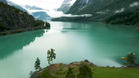 Drone-flying-with-low-hanging-clouds-over-turquoise-lake-Loen