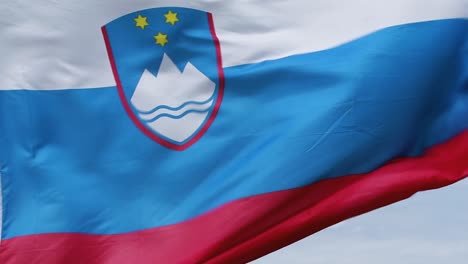 Primer-Plano-De-La-Bandera-Eslovena-Ondeando-En-El-Fuerte-Viento,-Con-Foco-En-El-Emblema-Nacional-Esloveno-Y-El-Cielo-Visible-En-El-Fondo