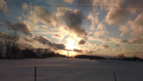 Wide-slow-moving-shot-of-beautiful-sunset-sky-overlooking-farmer's-fields-clad-in-snow