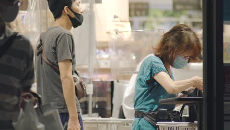 Arbeitspersonal-Und-Kunden,-Die-Während-Der-Covid-19-Gesichtsmasken-An-Der-Theke-Eines-Supermarktes-Mit-Plastikbarriere-In-Kamata,-Tokio,-Japan-Tragen