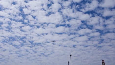 low-angle-view-of-single-engine-airplane-crossing-the-blue-sky-with-fluffy-clouds,-over-the-city