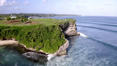 New-Kuta-Golf-Course-at-Dreamland-beach-in-Bali-Indonesia-near-ocean-cliff-with-waves-hitting-rocky-shore,-Aerial-Pedestal-rising-shot