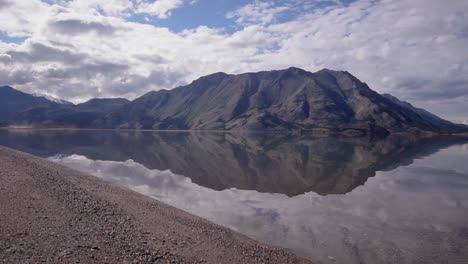 Wildnislandschaft-Sommerszene-Von-Yukon-Glänzender-Spiegel-Kluane-See-Durch-Braunen-Schluff,-Schmutz-Und-Steine-Am-Seerand-Und-Atemberaubender-Schafberg-Im-Hintergrund-An-Einem-Sonnigen-Blauen-Himmelstag,-Aufsteigende-Luft