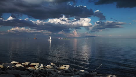 Weite-Aufnahme-Eines-Atemberaubenden-Seeblicks-An-Einem-Ruhigen-Tag-Mit-Vorbeifahrendem-Segelboot-Und-Reflexionen-Auf-Dem-Wasser