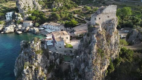 Aerial-flyover-beautiful-of-old-historic-village-Scopello-with-ocean-shore,cliffs-and-old-buildings-during-sunny-day-in-Italy