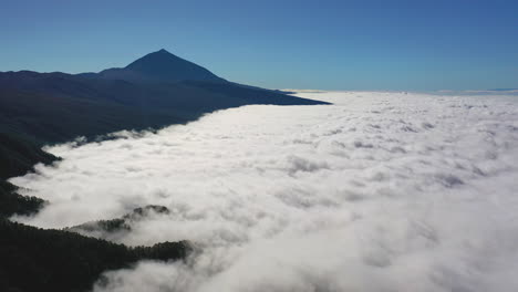 Aerial-shot-of-a-majestic-view-from-the-Pico-de-Teide-on-Canary-Islands-of-a-heavy-cloud-inversion-below-the-mountains-with-a-clear-blue-sky-above