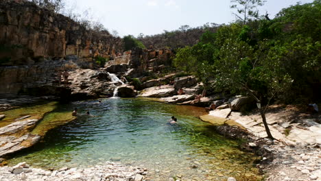 People-swimming-in-hidden-rocky-oasis-in-mountains,-wide-panning-shot