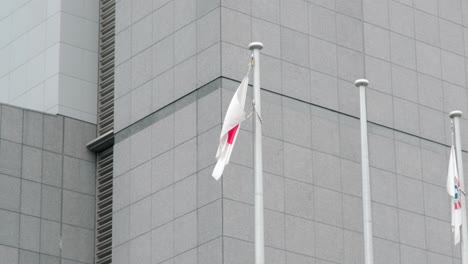 Bandera-Japonesa-Con-La-Bandera-De-La-Oficina-Regional-De-Inmigración-De-Tokio-Ondeando-En-El-Viento-Fuera-De-La-Oficina-Del-Gobierno-En-La-Ciudad-De-Minato,-Tokio,-Japón