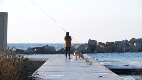 Young-man-walking-his-golden-retriever-dog-on-sea-dock-in-port-del-forum-barcelona-as-he-listens-to-music-on-his-headphones