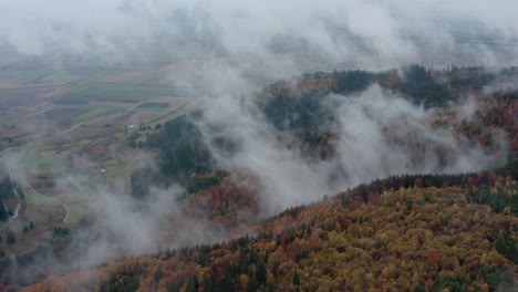 Drone-flight-over-hillside-with-cloud-forming-over-autumn-forest