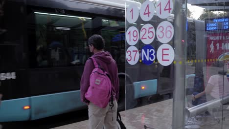 Bus-Kommt-An-Einer-Bushaltestelle-In-Malaga-City,-Spanien-An,-Mit-Passagieren-In-Masken,-Die-Warten---Coronavirus-New-Normal---Panning-Shot