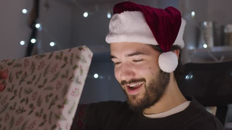 Männliches-öffnendes-Weihnachtsgeschenk,-Das-Aufleuchtet,-Während-Es-Eine-Weihnachtsmütze-Trägt