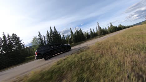 A-black-suv-filmed-driving-down-a-country-road-captured-from-a-side-angle-perspective-using-a-drone