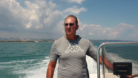 Caucasian-standing-man-driving-motorboat-with-coast-in-background