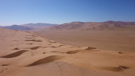 Aerial-landscape-shot-of-the-golden-dry-sand-and-mountainous-horizon-of-the-Atacama-desert,-bright-sunlight